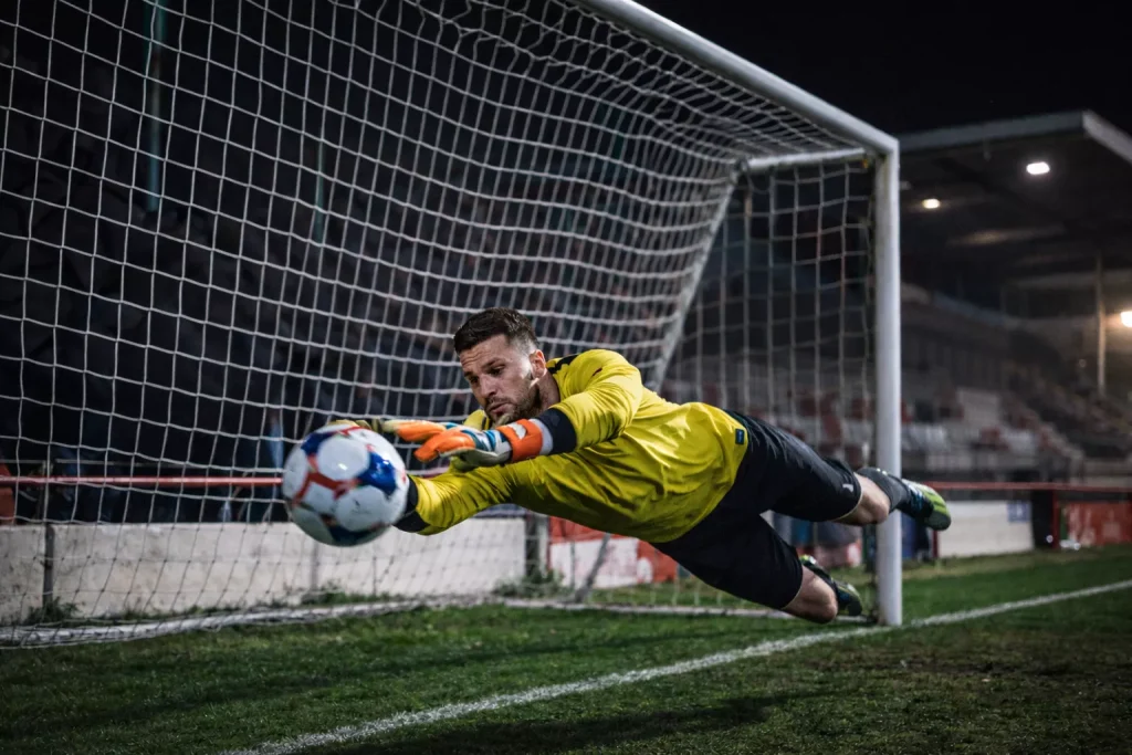 Portero de fútbol lanzándose para atrapar un balón en un estadio pequeño lleno de público